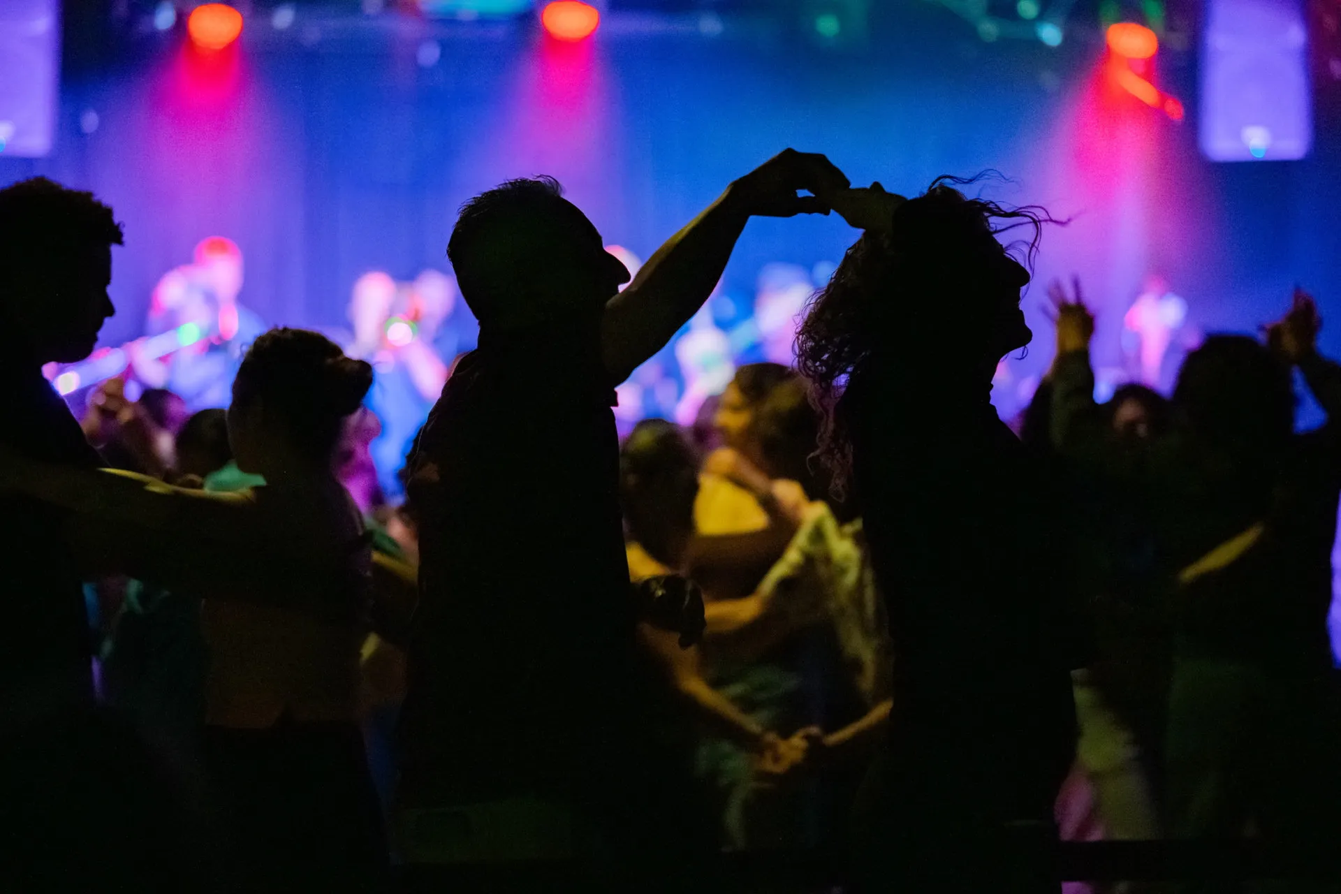 Silhouetted dancers turning beneath colorful club lights.